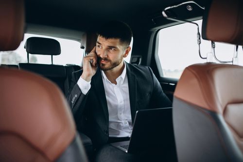 A man sits in the back of a luxury executive SUV, holding a phone to his ear and taking a business call during a professional chauffeur service from Orange County to and from LAX.