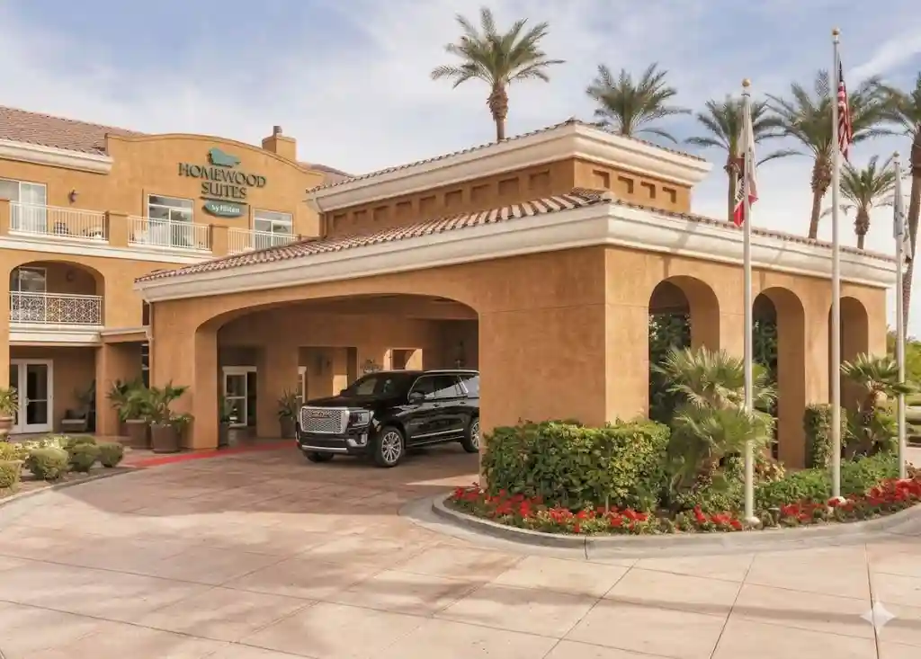 A pristine, black luxury GMC Yukon SUV from South Bay Transportation Services is parked under the elegant front portico of the Homewood Suites by Hilton, providing executive hotel transfer services.